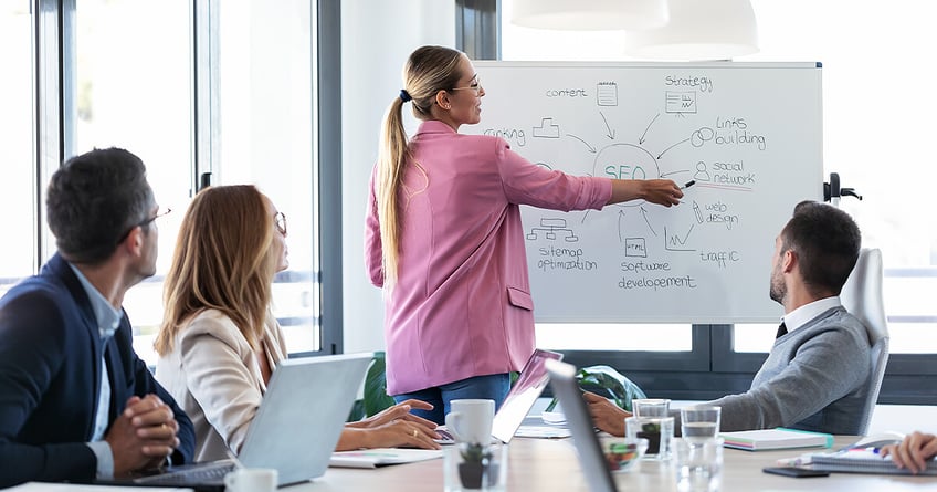 Business woman showing SEO strategies on whiteboard to team