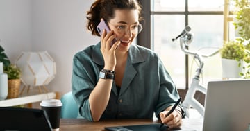 Woman on the phone and happily looking at her computer