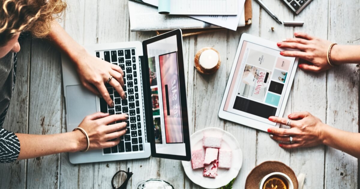 Hands on a laptop and tablet with coffee and papers making money on a website