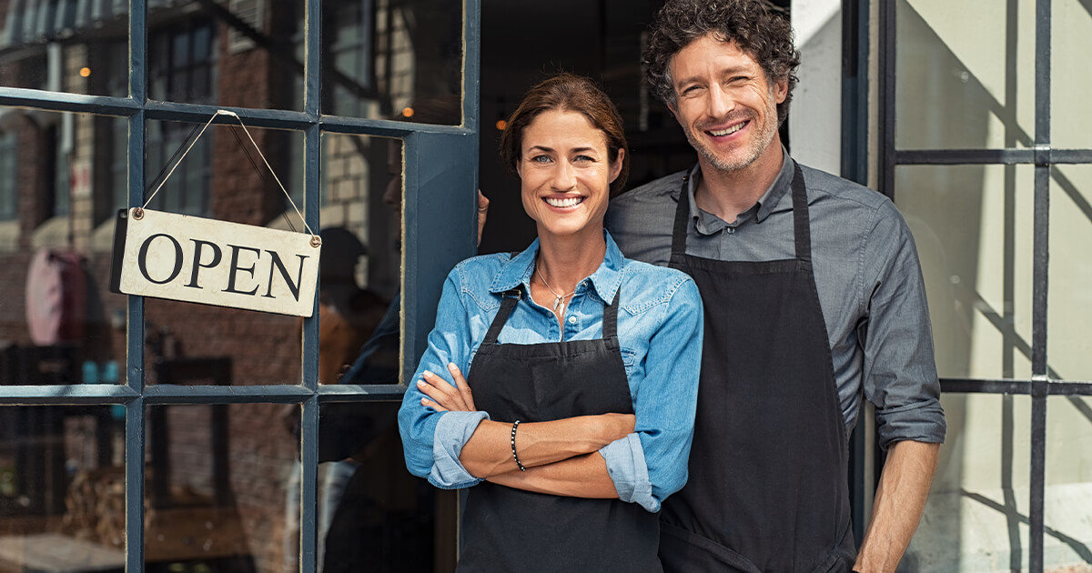 Business owners standing in front of open sign at store front